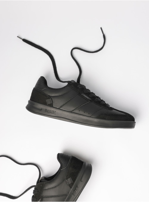 Zapatilla urbana unisex de cuero sintético negro con diseño total black y texturas oscuras.