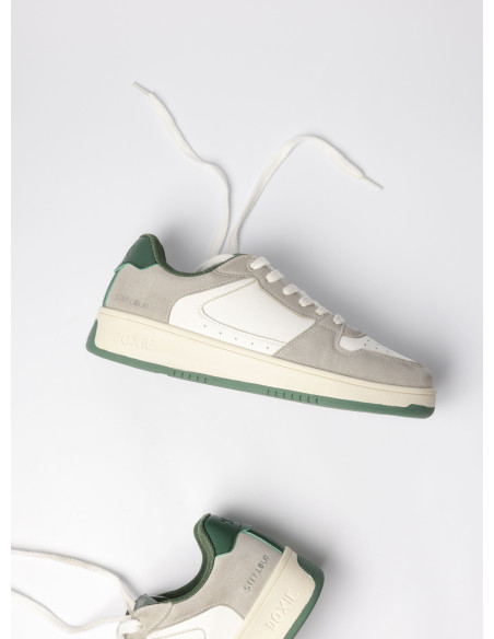 Zapatilla con acentos verdes sobre base gris, diseñada para un look contemporáneo y versátil en entornos urbanos.