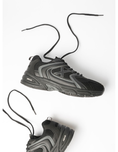 Vista lateral de zapatilla negra unisex con diseño moderno y suela de perfil marcado.