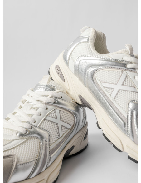 Perspectiva de zapatilla unisex en color plata, resaltando su estética llamativa y moderna.